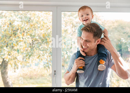 Bébé garçon sur les épaules du père à la maison par fenêtre Banque D'Images