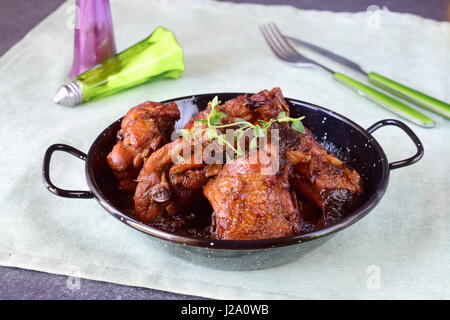 Poulet aux pruneaux cuits au four dans un bol noir sur un fond textile. Banque D'Images