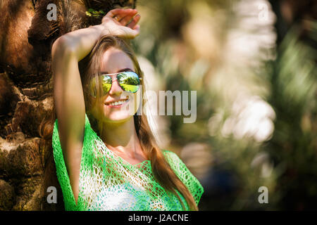 Portrait d'une jeune femme en lunettes de soleil dans un jardin tropical Banque D'Images