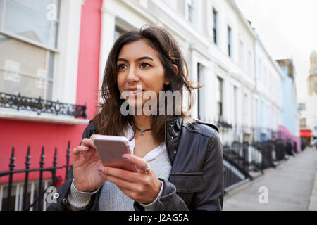 Young woman using mobile phone in residential city street Banque D'Images