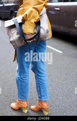 Londres - Février 2017 : femme portant des jeans et blouson de cuir jaune, tenant un grand sac à main dans la rue pendant la Semaine de la mode de Londres, vertical Banque D'Images