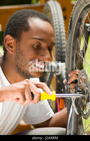 Homme portant une chemise blanche de travail concentré sur la réparation de la mécanique à l'aide de l'outil tournevis bicyclette Banque D'Images