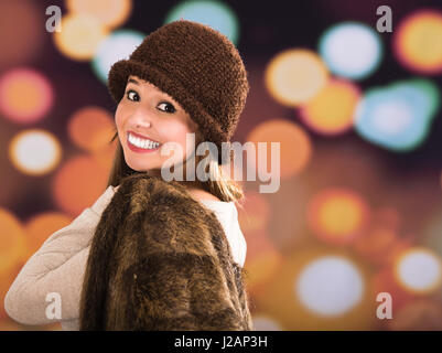 Jolie jeune femme brune fourrure Veste style, bonnet et écharpe posant joyeusement avec une lumière floue fond gouttes Banque D'Images