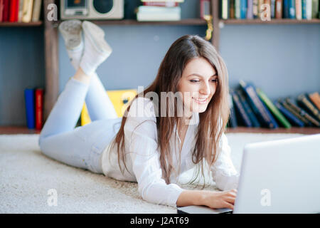 La belle jeune femme étendue sur le sol avec ordinateur portable. Banque D'Images