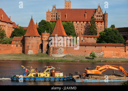 La Pologne, château de Malbork (Marienburg) de l'Ordre des Chevaliers teutoniques, tugboat pushing excavatrice sur chaland avec la Rivière Nogat Banque D'Images