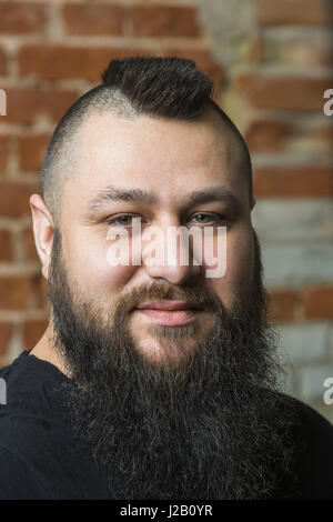 Close-up portrait of confident hairdresser avec barbe contre mur de brique au salon de coiffure Banque D'Images