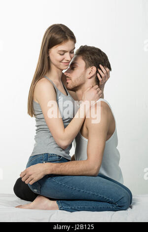 Couple romantique tout en étant assis sur le lit contre fond blanc Banque D'Images