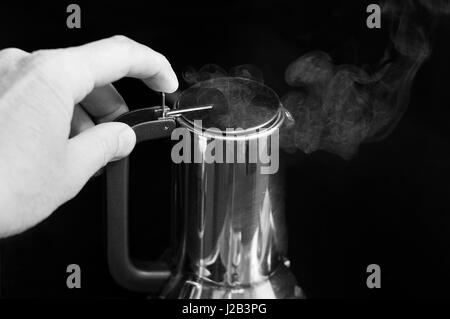La main de l'homme tenant une bouilloire avec de la vapeur qui sort, en noir et blanc Banque D'Images