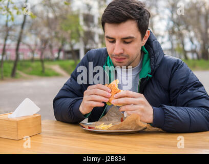 L'homme de manger un hamburger dans street food cafe Banque D'Images