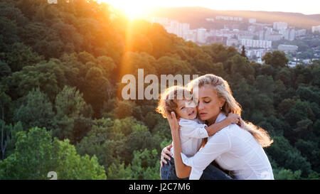 Jeune belle mother hugging son petit fils. Belle vue sur la nature. Banque D'Images