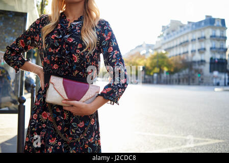 Les femmes en robe à fleurs sac d'embrayage holding, mid section Banque D'Images