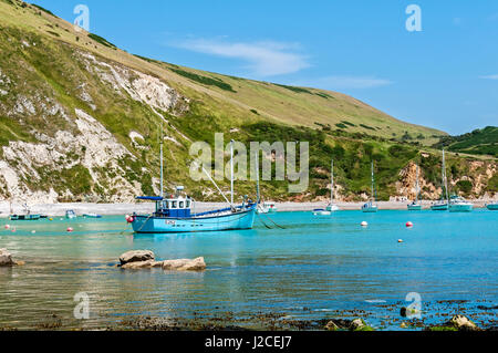 Le soleil brille sur un bateau de pêche amarré avec d'autres bateaux de plaisance et yachts sur l'eau bleue de crique de lulworth cove entourée par des falaises Banque D'Images