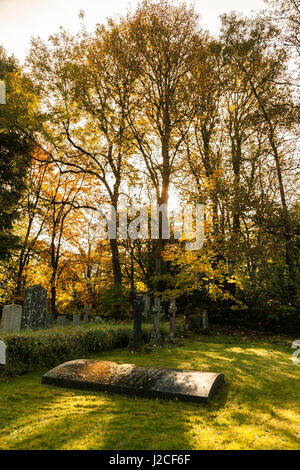 La lumière brille à travers les arbres au coucher du soleil sur une tombe dans le cimetière de l'église Holy Trinity à Pitlochry. Le Perthshire, Écosse. Banque D'Images