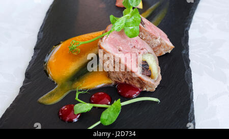 Filet de porc rôti, farci aux pommes et pruneaux, servi avec sauce aux canneberges et orange douce, sur une plaque d'ardoise noire . Banque D'Images