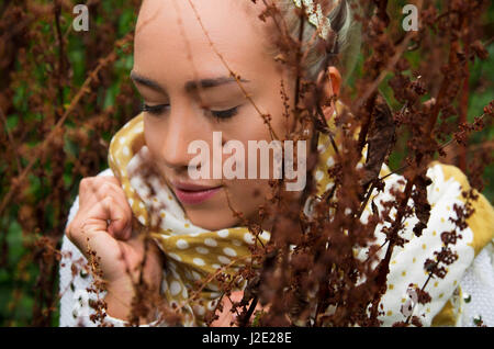 Belle jeune fille latine derrière certaines mauvaises herbes forestières Banque D'Images