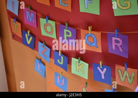 Mur de la maternelle avec des lettres colorées faites de carrés de papier sont suspendus à partir de fils multicolores sur un mur rouge et orange Banque D'Images