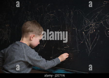 Vue arrière de l'école élémentaire mâle élève écrit sur le tableau noir Banque D'Images