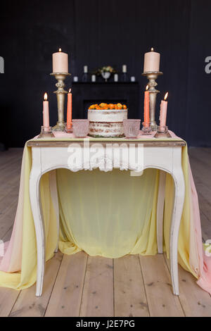 Gâteau de mariage, des bougies dans les chandeliers et deux verres sur une table vintage blanc décoré avec un chiffon. Photo verticale à sa pleine grandeur. Banque D'Images