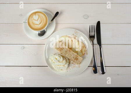 Une tasse de Cappuccino et un morceau de délicieux strudel aux pommes sur l'assiette blanche sur une table en bois blanc. La vue d'en haut Banque D'Images