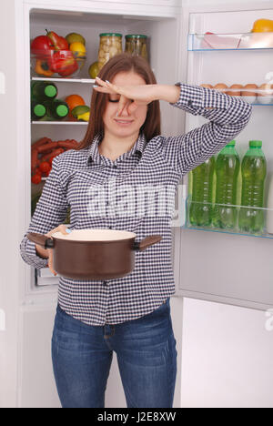 En colère et bouleversé à la femme au foyer dans un pot avec un repas. Belle jeune fille près du réfrigérateur. Banque D'Images