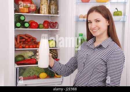 Jeune fille tenir une bouteille de lait, debout près de l'Open d'un réfrigérateur dans la cuisine Banque D'Images