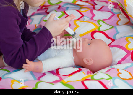 Little girl playing doctor avec une poupée et l'application de médicaments avec seringue et en prenant soin d'une poupée, de concept et de l'enfance, les habitudes de vie de la maternité Banque D'Images