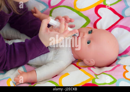 Little girl playing doctor avec une poupée et l'application de médicaments avec seringue et en prenant soin d'une poupée, de concept et de l'enfance, les habitudes de vie de la maternité Banque D'Images