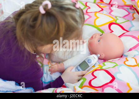 Little girl playing doctor avec une poupée, mesure de la température électronique avec themometer et prendre soin d'une poupée, maternité, mode de vie et concept c Banque D'Images