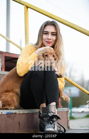 Belle blonde à la recherche comme Jennifer Aniston assis avec un Cocker chien sur un escalier métallique Banque D'Images