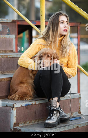 Belle blonde à la recherche comme Jennifer Aniston assis avec un Cocker chien sur un escalier métallique Banque D'Images