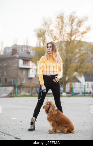 Belle blonde à la recherche comme Jennifer Aniston est debout avec chien contre fond de maisons urbaines Banque D'Images