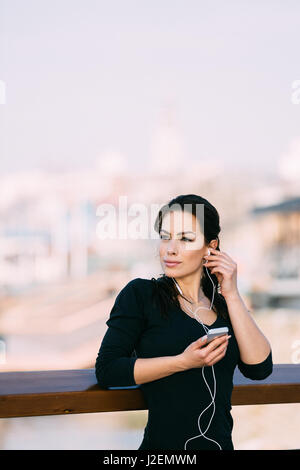 Young smiling belle fit woman using smartphone tout en se reposant après ses exercices et écouter de la musique. Concept de remise en forme, ajouté des grains filtre. Banque D'Images