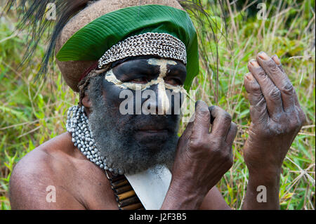 Habillés de couleurs vives chef tribal local peignant son visage dans les hautes terres de la Papouasie-Nouvelle-Guinée, la Mélanésie Banque D'Images