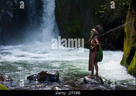 Habillés de couleurs vives et peint chef tribal local se tient devant une chute d'eau dans les hautes terres de la Papouasie-Nouvelle-Guinée, la Mélanésie Banque D'Images