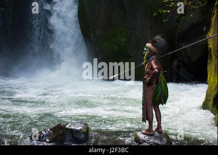 Habillés de couleurs vives et peint chef tribal local se tient devant une chute d'eau dans les hautes terres de la Papouasie-Nouvelle-Guinée, la Mélanésie Banque D'Images