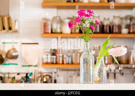 Fleurs dans deux vases dans une cuisine blanche avec étagères en bois pourvue d'épices. Violet, fuchsia, rose et fleurs. Banque D'Images