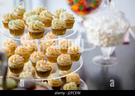 Vanilla bean mini cupcakes décorés de perles bonbon rose et cyan clair sur les niveaux bac sur une table de dessert avec des guimauves, jujubes, et macarons Banque D'Images