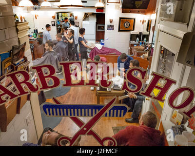 Les barbiers des deux sexes servent une clientèle occupé à un salon de coiffure à Brooklyn Heights, New York City, alors que les clients attendent leur tour. Banque D'Images