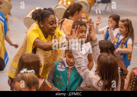 Multiraciale enthousiaste des éclaireuses se plonger dans l'esprit d'un atelier de vente de biscuits à Irvine, CA, en dansant avec un afro-américain high school étudiant en théâtre habillés en costume d'un cookie. Banque D'Images