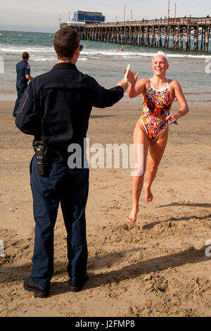 Une jeune femme adulte à l'investiture pour l'été un sauveteur emploi à Newport Beach, CA, s'étend de la surf et atteint pour un stick signifiant l'achèvement de sa nage admissible. Remarque Newport Pier en arrière-plan. Banque D'Images