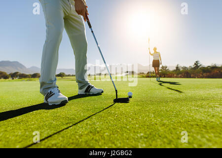 Low angle view of golfeur sur putting green sur le point de prendre la photo. Homme joueur de golf putting on vert avec deuxième joueuse dans l'arrière-plan vertige Banque D'Images