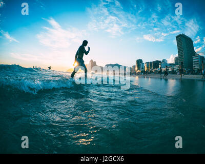 RIO DE JANEIRO - Fevrier 2, 2013 : un jeune Brésilien promenades à travers les vagues sur le rivage de la plage d'Ipanema en face du soleil couchant. Banque D'Images