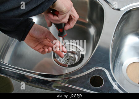 Travailleur de la construction d'installer les tubes de vidange d'un évier de cuisine en acier inoxydable. Banque D'Images