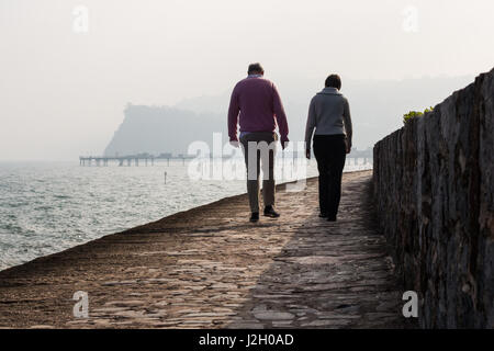 Un homme et une femme à pied le long du chemin de fer avant la mer Teignmouth avec la jetée et l'OCIM des roches dans l'arrière-plan. Banque D'Images