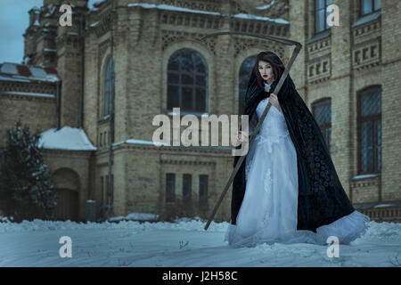 Jeune fille dans une robe de mariage tenant une faux de la mort. Il frappe la peur et la terreur. Banque D'Images