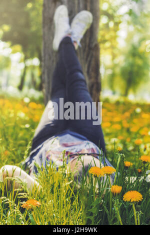 Femme couchée dans le champ d'herbe rempli de fleurs jaunes, des jambes jusqu'aux trois Banque D'Images