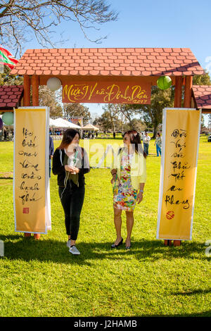 Dans un Fountain Valley, CA, parc, deux femmes vietnamienne américaine à pied par la porte d'un village vietnamien 'impromptu' pour célébrer le Nouvel An lunaire ou Tet. Remarque Vietnanese écrit sur les panneaux. Banque D'Images