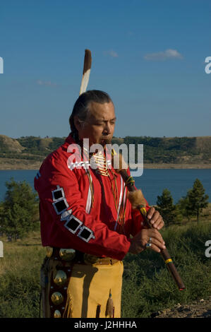 Habillé en costume traditionnel de jambières en peau de daim, breechcloth et ruban rouge shirt est native flute player Keith Bear (Mandans) avec la rivière Missouri, dans l'arrière-plan sur la réserve indienne de Fort Berthold des Trois tribus affiliées, ND Banque D'Images