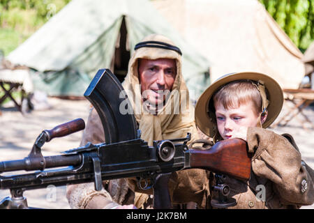 Salute to the 40s re-enactment. Enfant, garçon blond, 6-7 ans, en uniforme de l'armée britannique, étant montré comment fire la mitrailleuse Bren par Desert Rat soldat. Banque D'Images