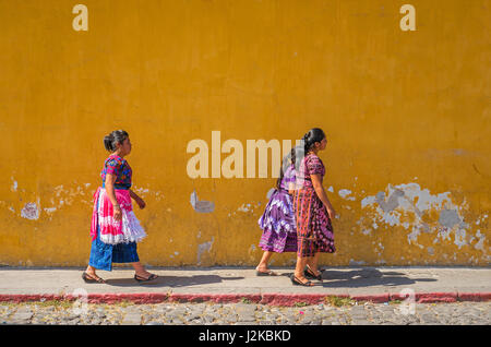 Les femmes mayas marche dans la rue avec un mur jaune coloré comme arrière-plan dans le centre-ville d'Antigua, Guatemala. Banque D'Images